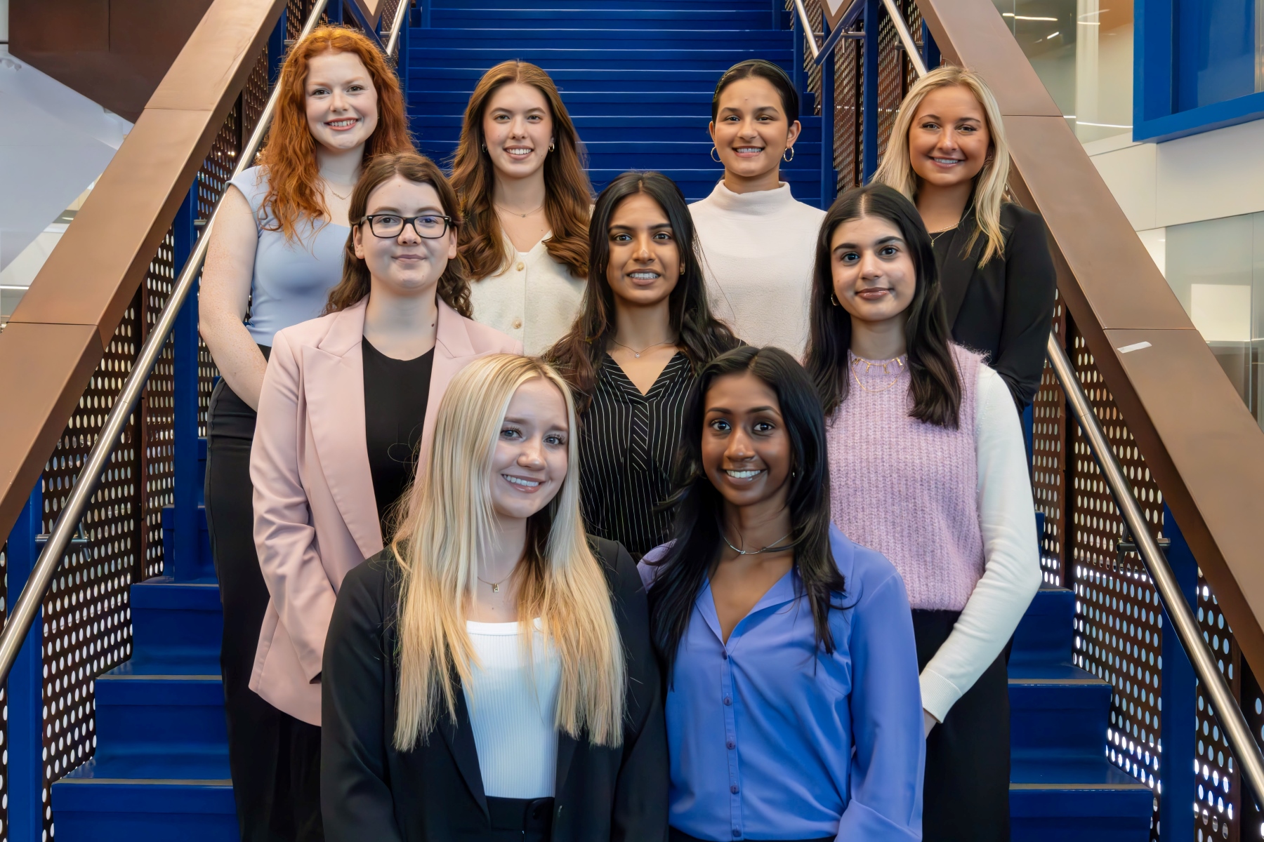 The executive team of the University of Kansas Women in Finance program poses for a photo on a blue staircase. 