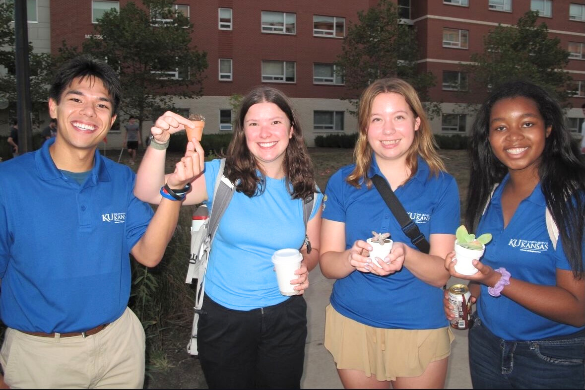 Four University of Kansas resident assistants at an event, holding tiny potted plants.