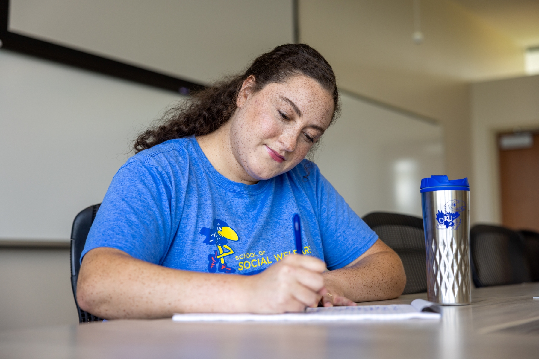 University of Kansas MSW alumna Sydnee Bradley writes at a desk in a classroom. 