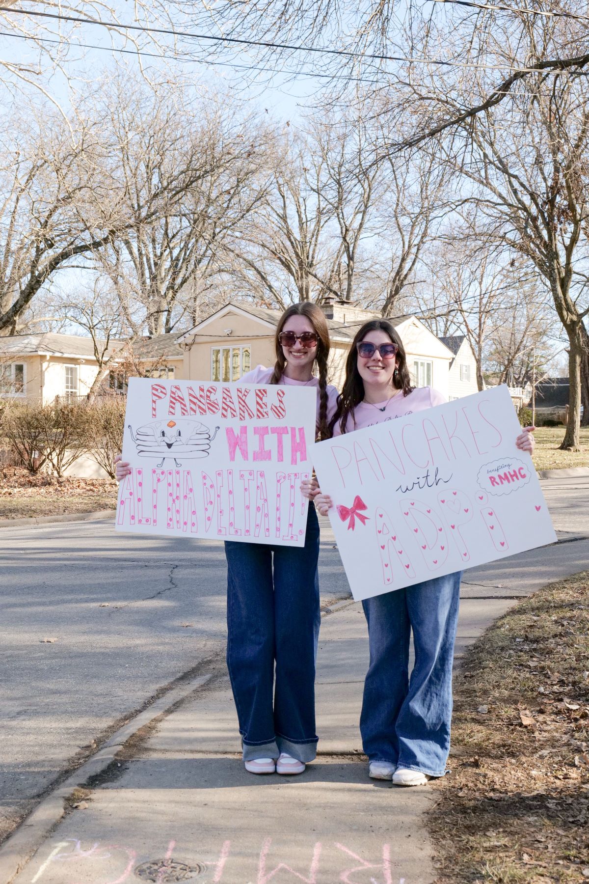 Two sorority women hold signs advertising a philanthropic pancake themed event on the University of Kansas campus.