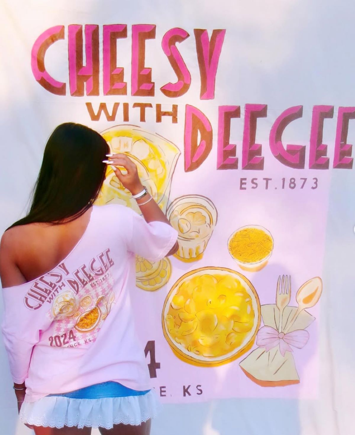 A woman paints a "Cheesy with Deegee" sign for a University of Kansas sorority philanthropy event. 