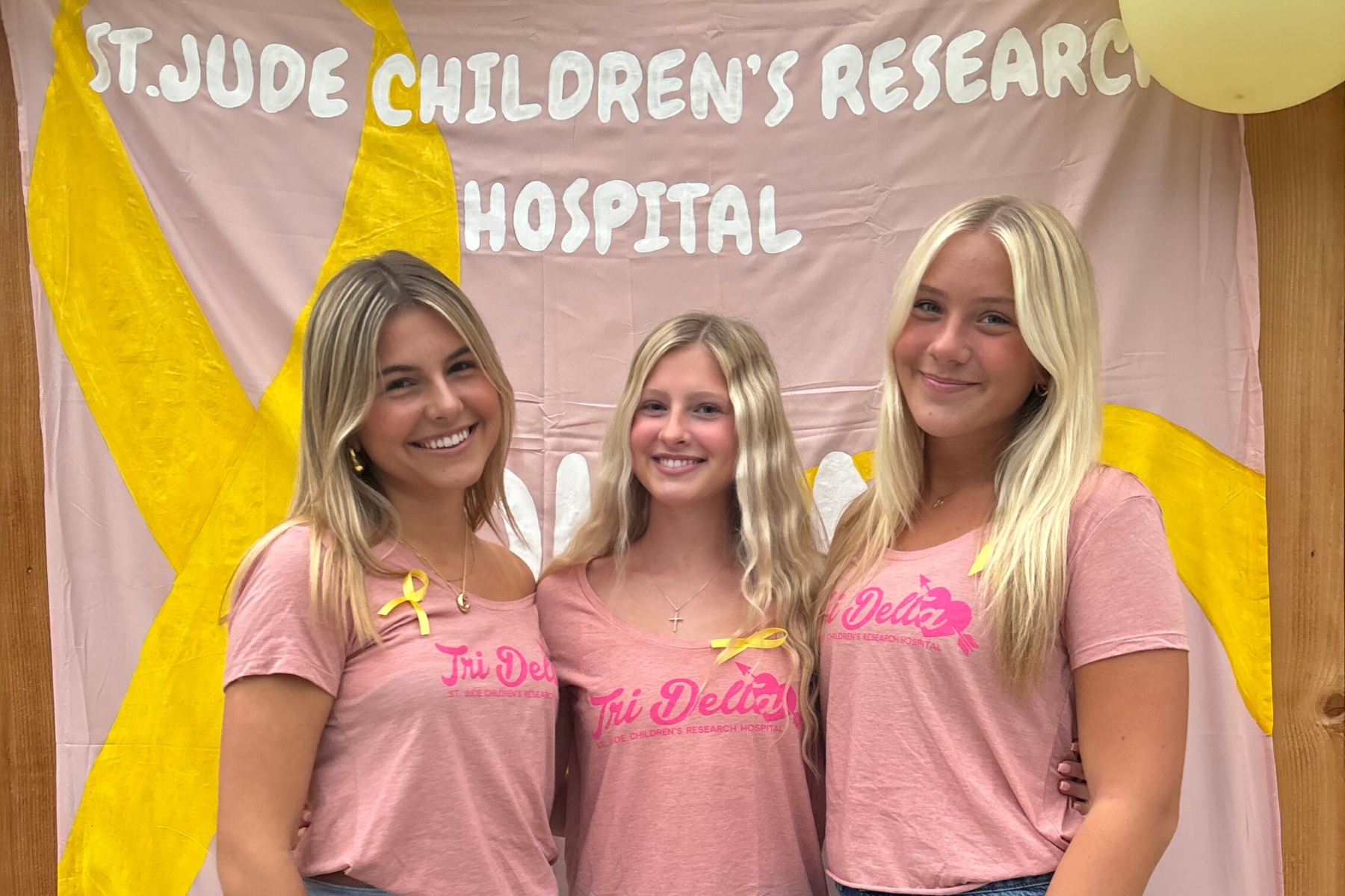 A group of sorority women pose underneath a sign for St Jude's Children's hospital during a philanthropy event.