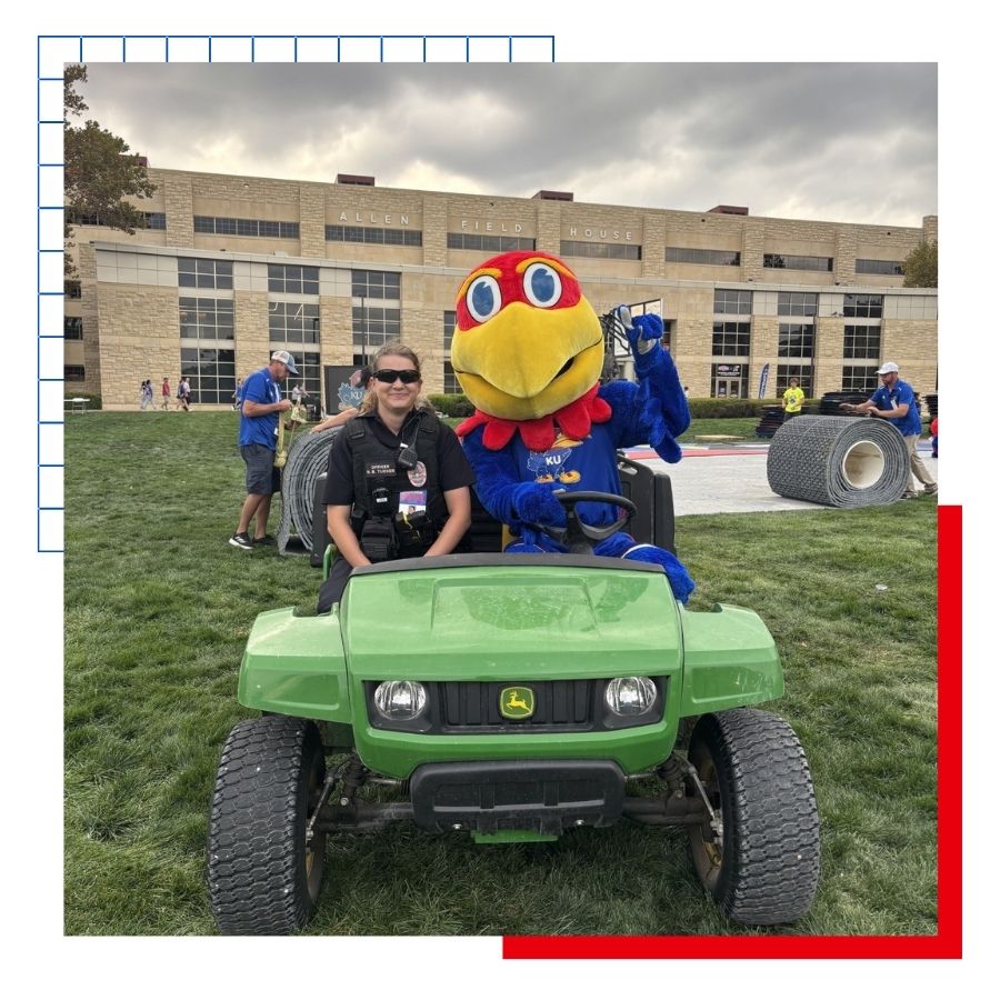 A University of Kansas police officer rides in a side by side John Deere with the Jayhawk mascot.