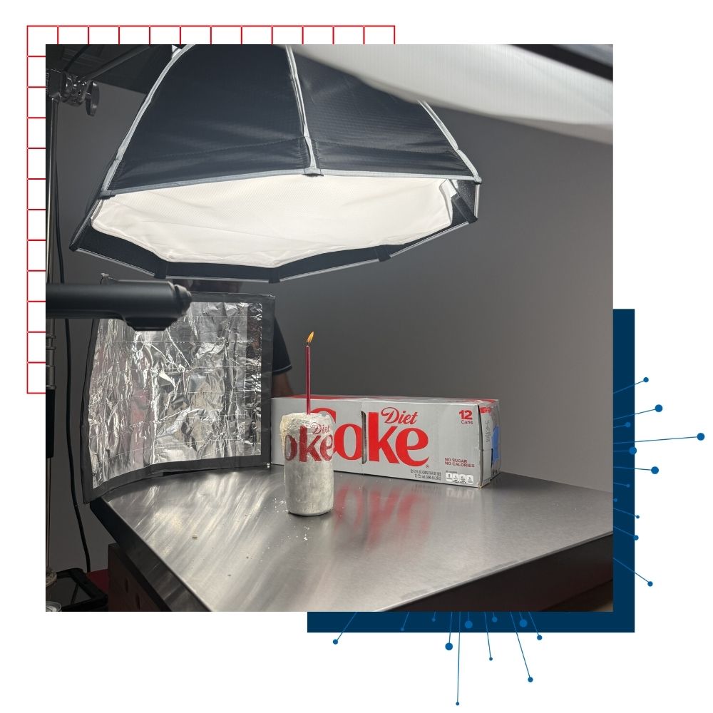 A photo studio set up with a product shot of Diet Coke with a candle, and a 12 pack of diet coke in the background.