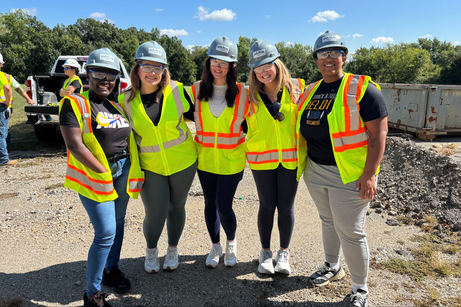 University of Kansas MPA students gather for a group photo while wearing high visibility vests and hard hats at a construction site for a school event. 