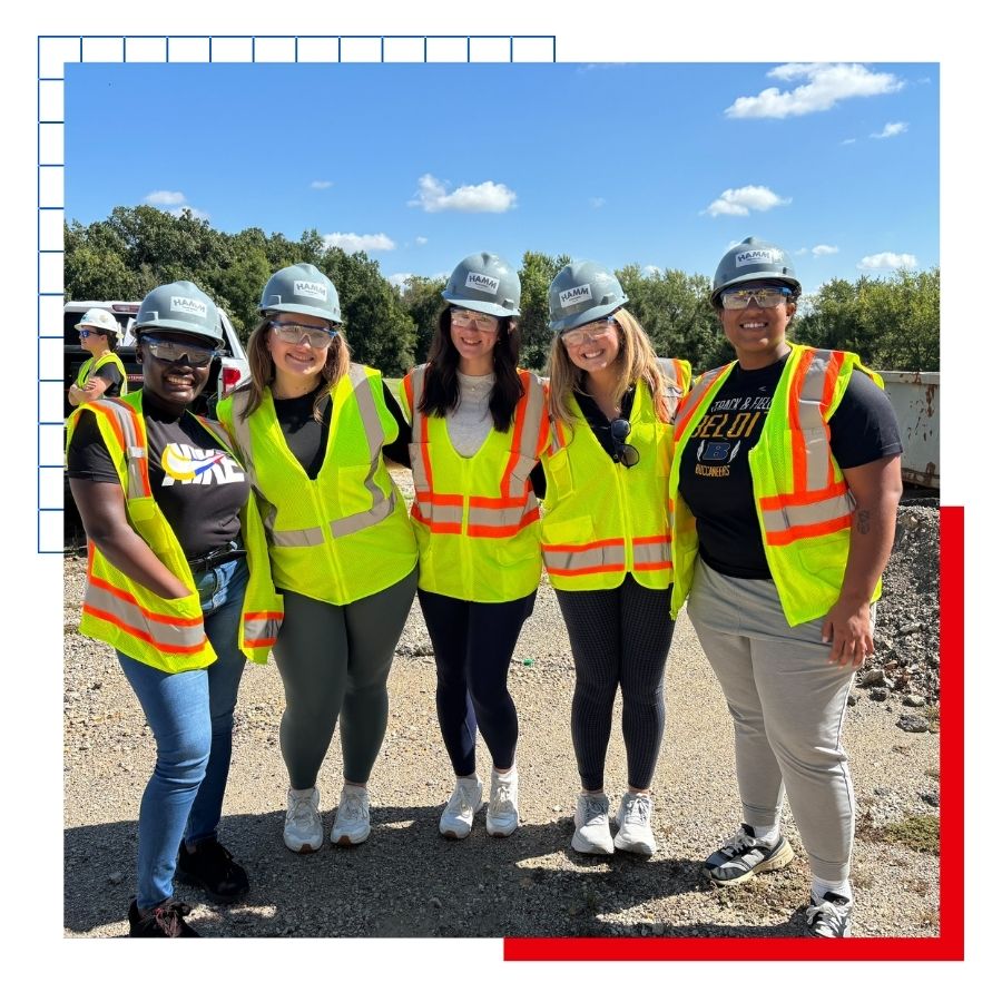 KU Masters of Public Administration students pose for a photo wearing hard hats and high visibility vests at a construction site. 
