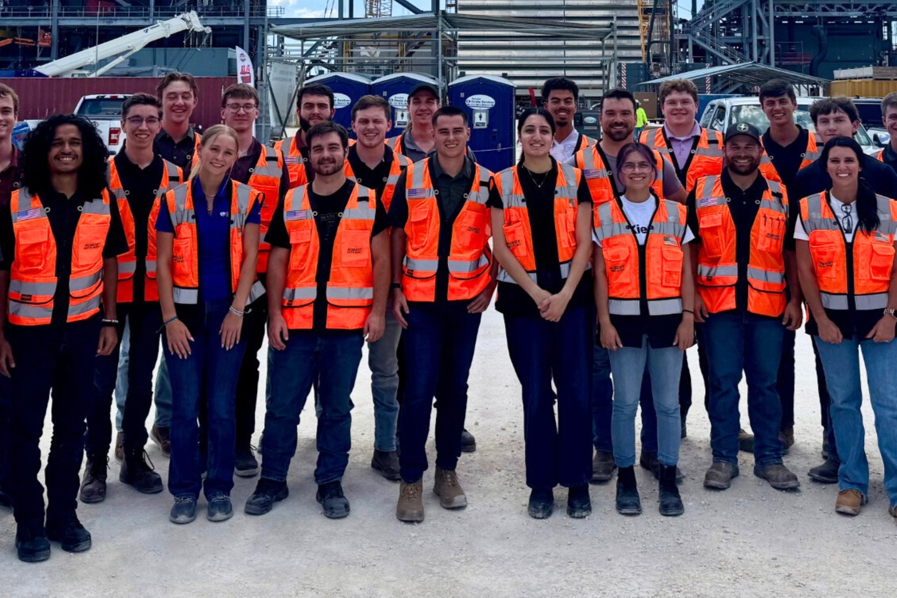 A group of college interns pose for a picture in orange safety vests. 