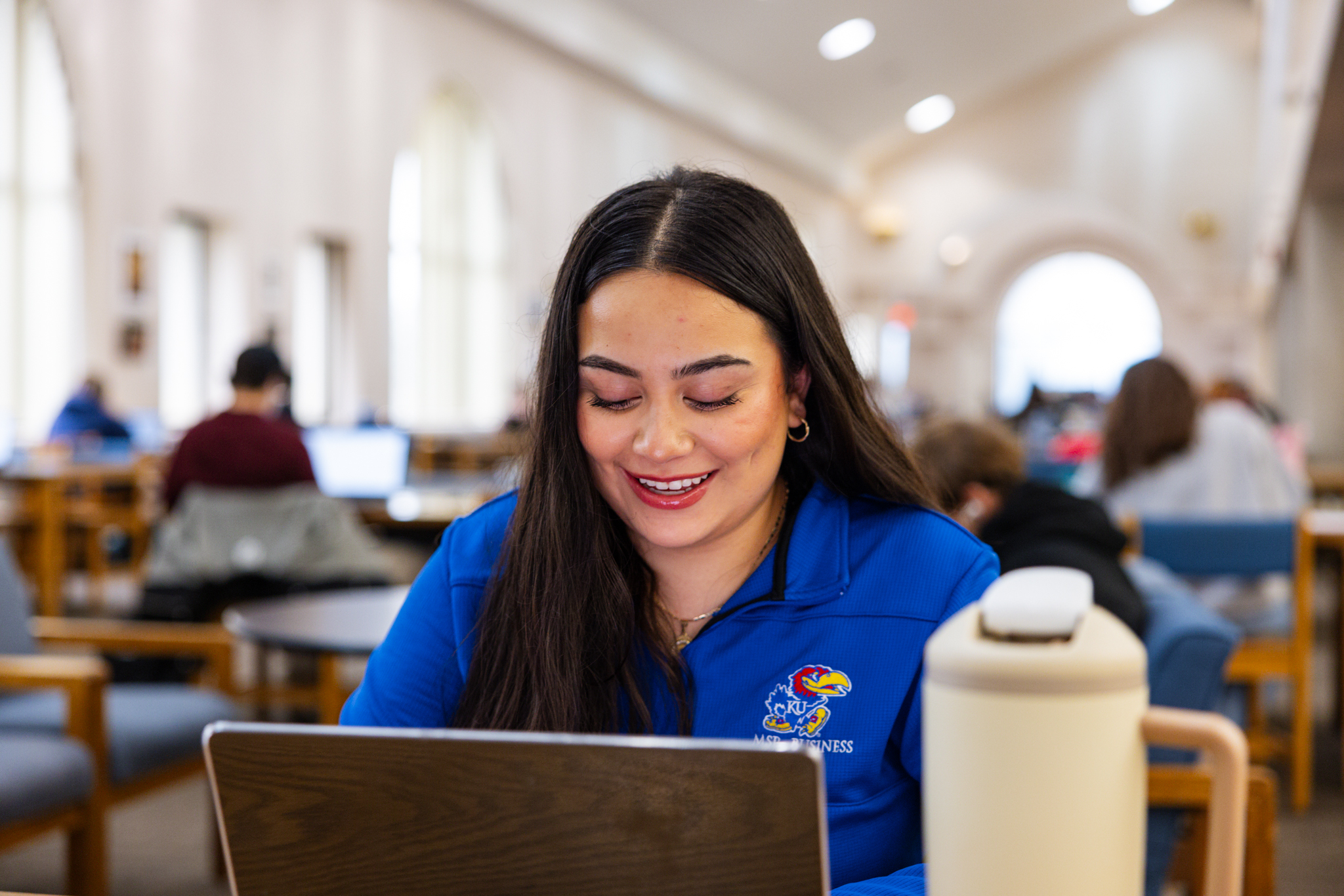 A KU student types at a laptop in a campus library, working on a resume for an internship application.