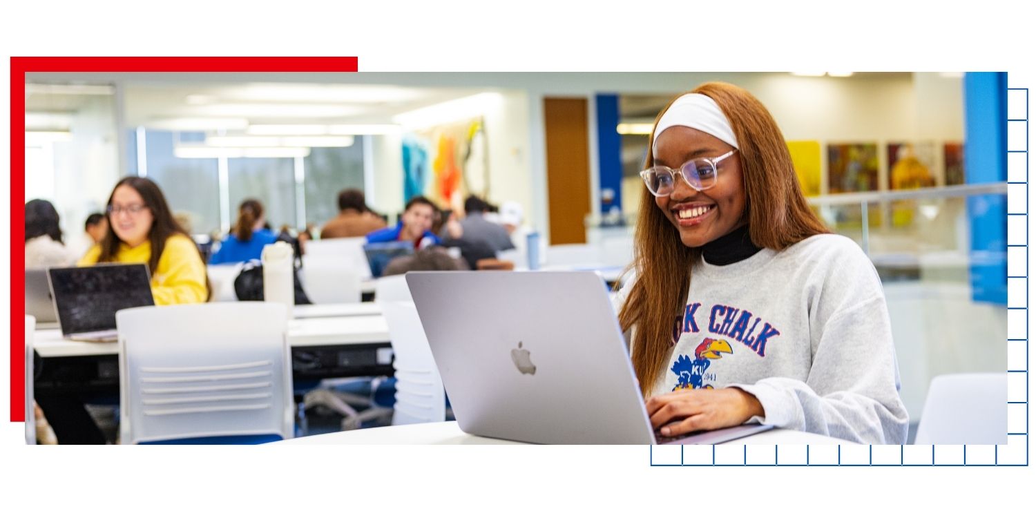 A University of Kansas college student types at a laptop in a campus building.