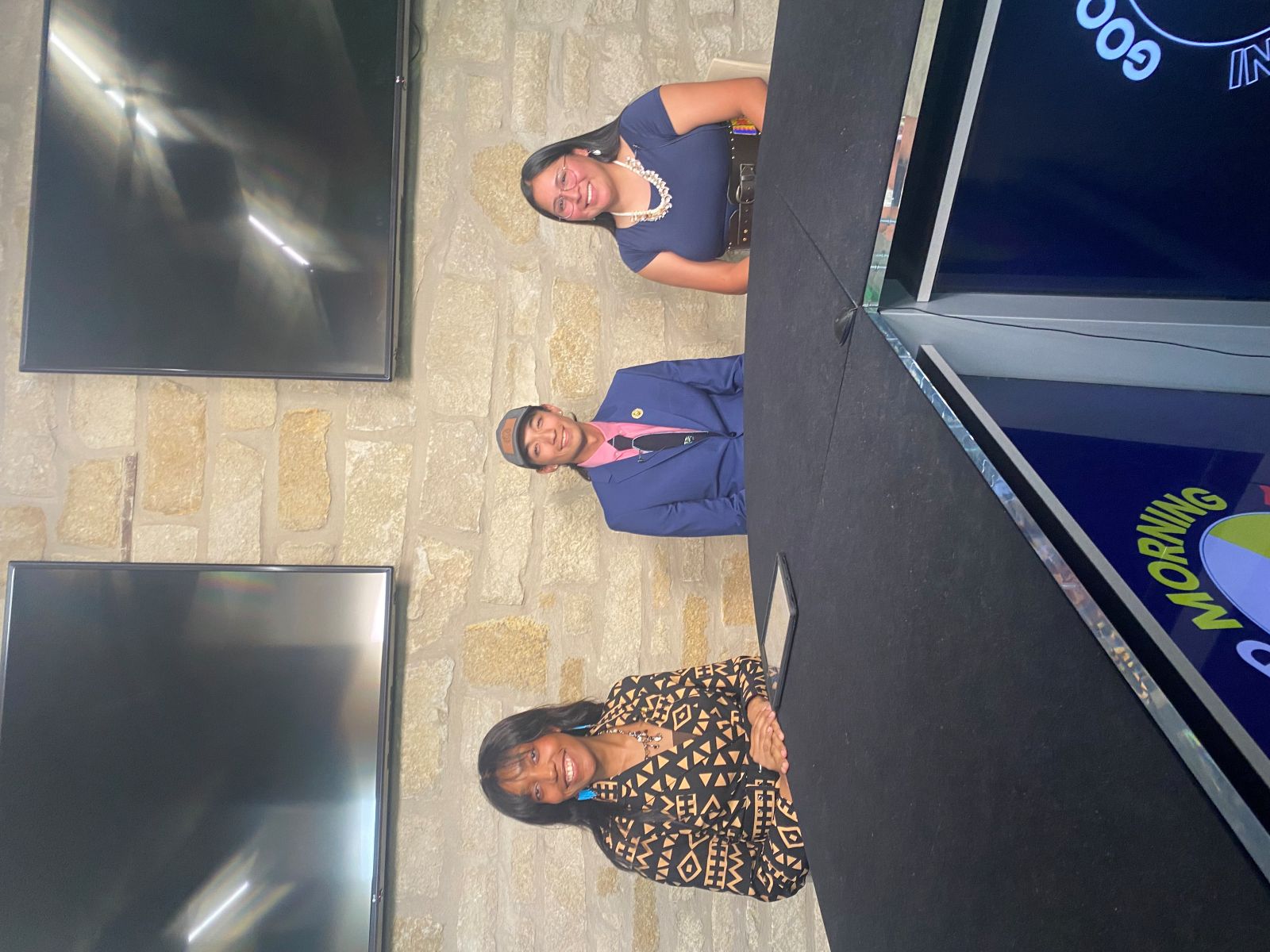 University of Kansas students sit behind the desk of the production studio in the KU School of Journalism to film Good Morning Indian Country. 