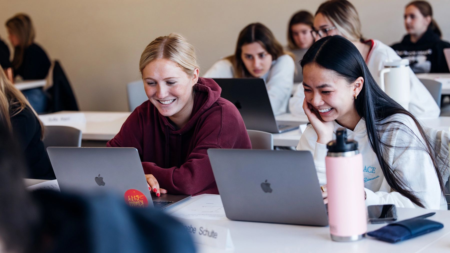 Two students on laptop computers in a classroom setting at the University of Kansas School of Business.