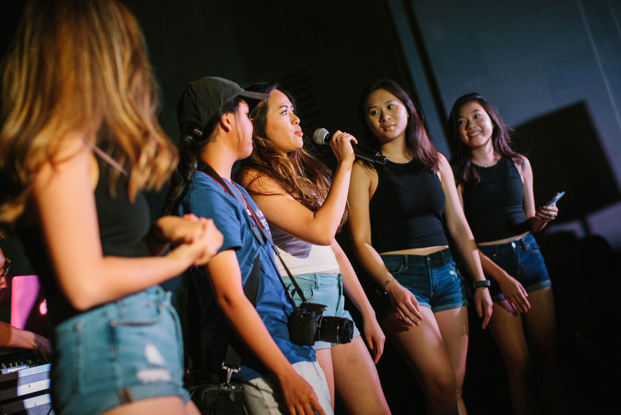 5 KU students stand on stage at the Office of Multicultural Affairs block party, an event at KU's Hawk Week. One of them is speaking into a microphone.